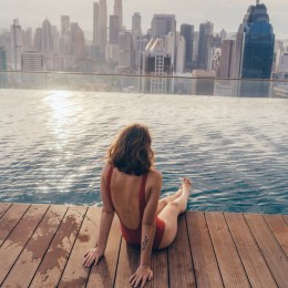 Young Caucasian woman in the swimming pool with view of Kuala Lumpur