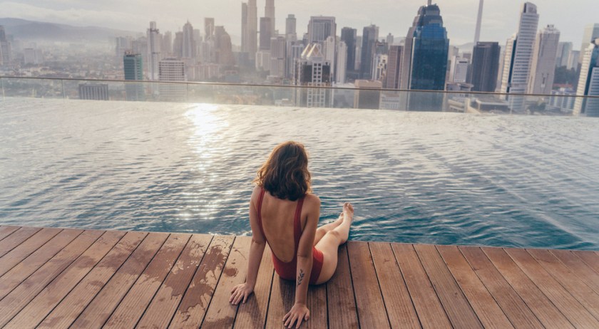 Young Caucasian woman in the swimming pool with view of Kuala Lumpur