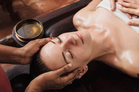 Ayurvedic face massage with oil on the wooden table AWE Cosmeceuticals